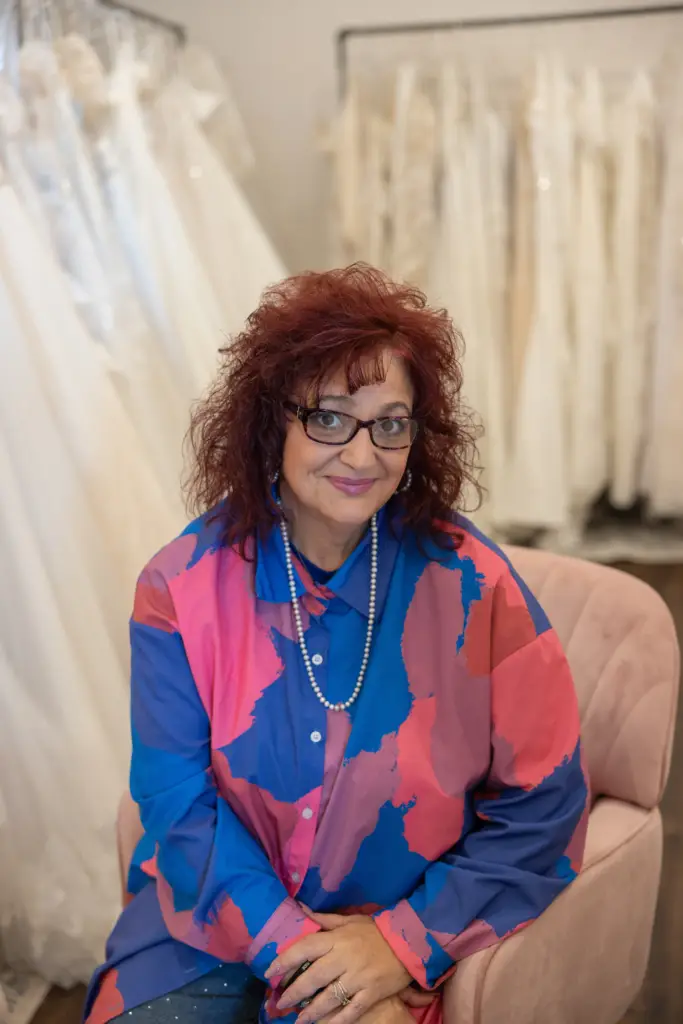 Bridal stylist seated in a wedding dress showroom surrounded by elegant bridal gowns