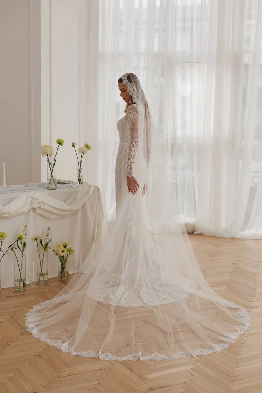 Side profile of bride wearing a lace fitted wedding dress with long sleeves and flowing cathedral veil.