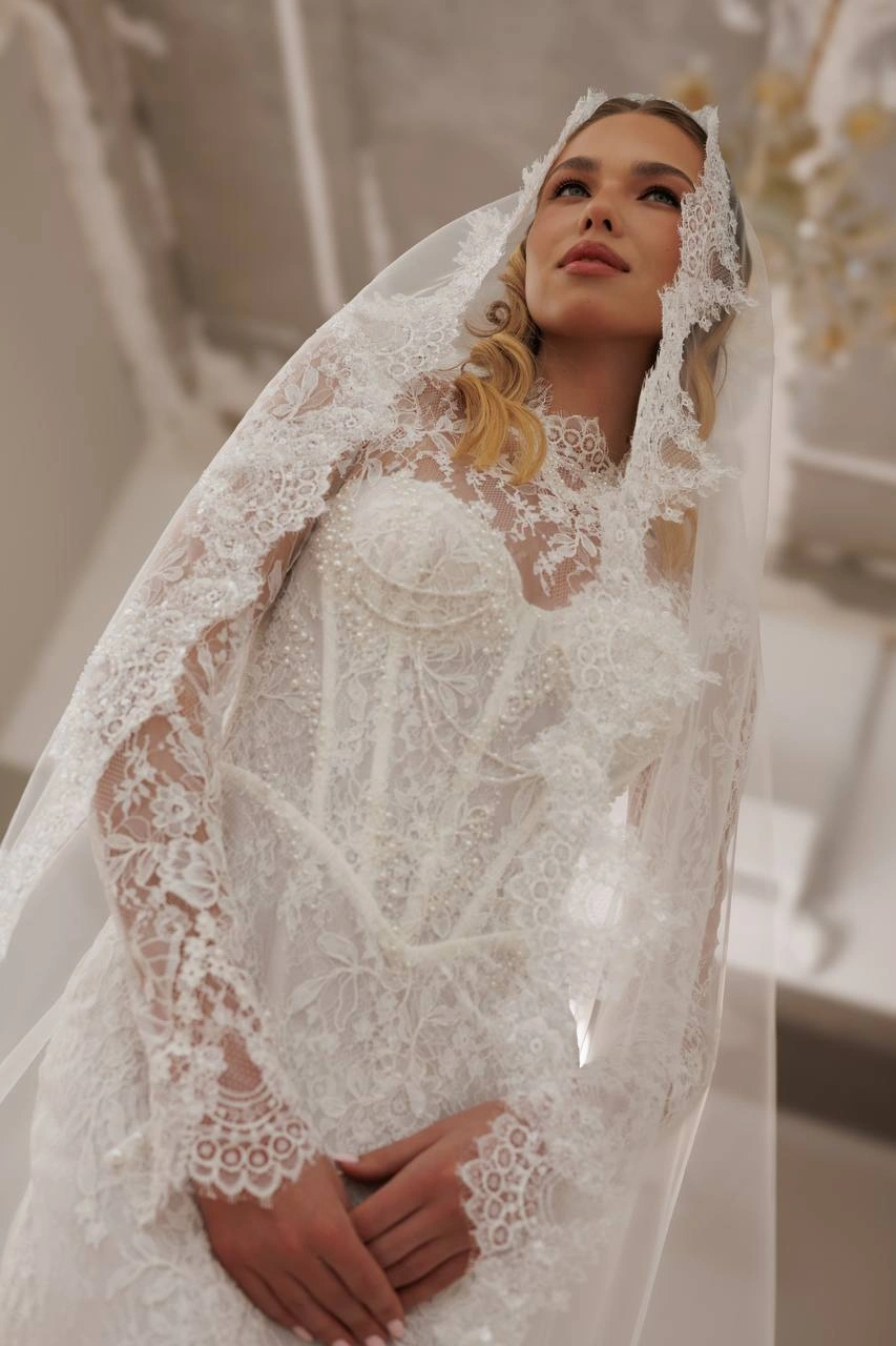 Close-up of bride wearing an intricate lace wedding dress and lace-trimmed bridal veil.