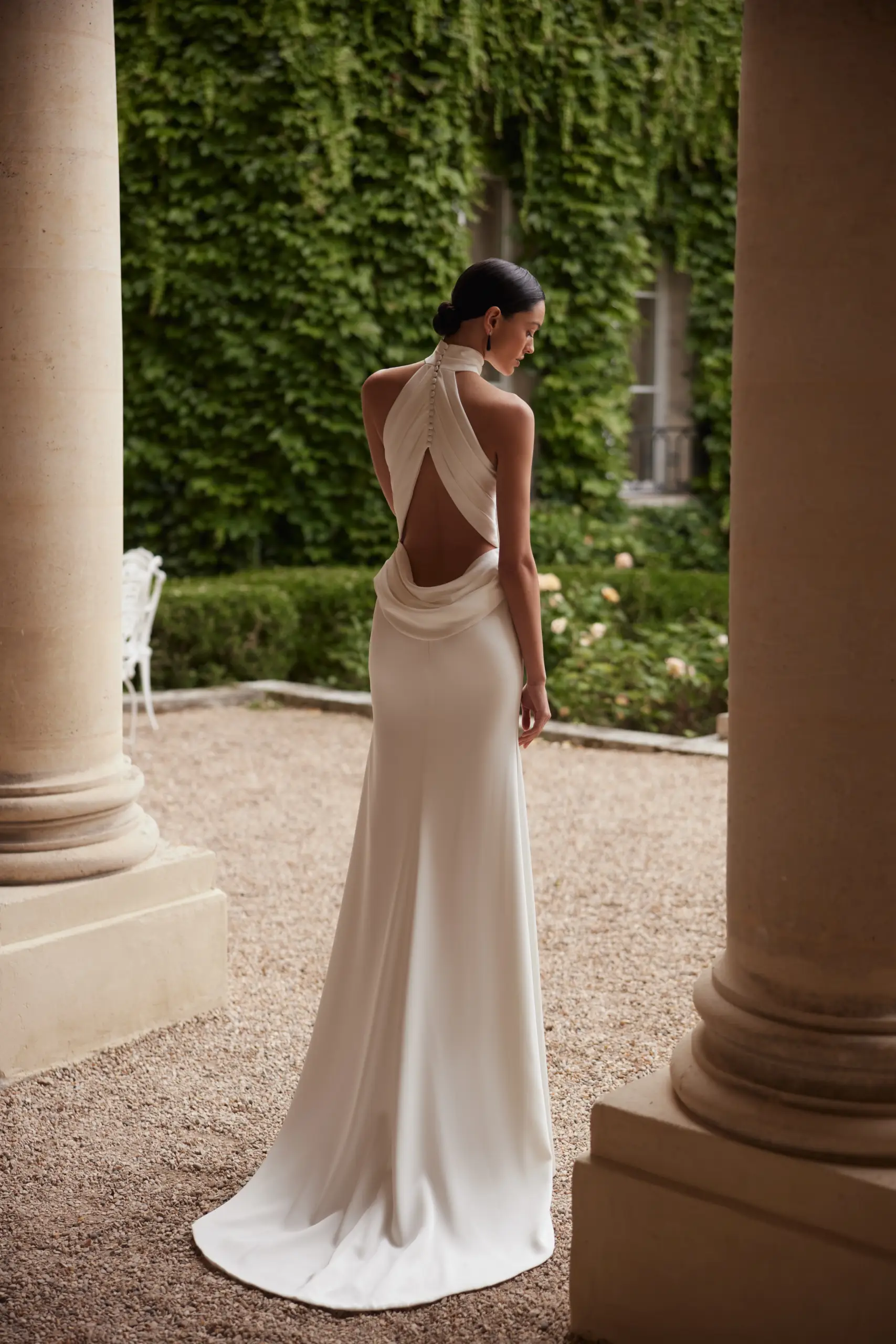 Bride wearing a backless halter wedding dress with elegant draping and a flowing train.