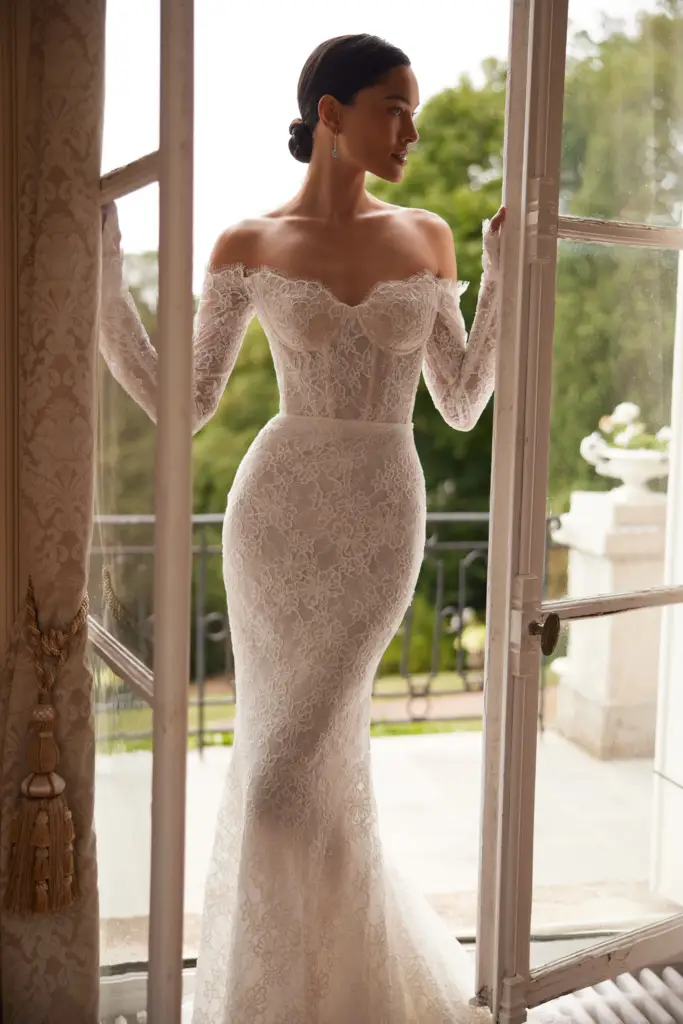 Bride wearing an off-the-shoulder lace wedding dress with long sleeves and floral lace details.