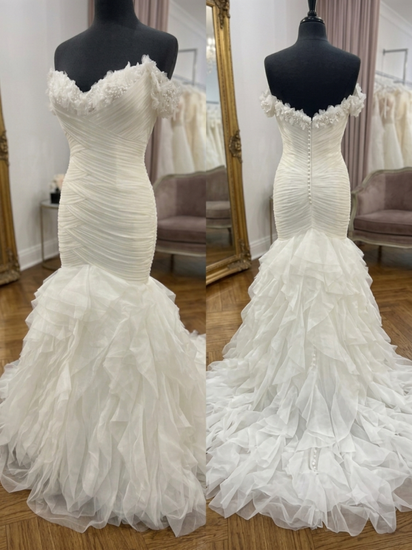 Private Label "Penelope" mermaid wedding dress on a mannequin in a luxury boutique, showcasing the off-the-shoulder 3D floral neckline, criss-cross ruched tulle bodice, and voluminous ruffled skirt.