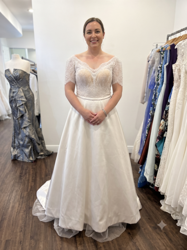 Front full-length view of the Private Label "Ariana" A-line wedding dress in size 12, featuring a beaded lace short-sleeve bodice and a structured ivory satin skirt.