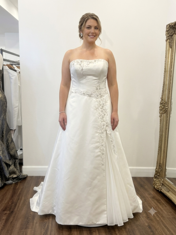 Professional front and back showcase of the private label Scarlett size 14 strapless wedding dress, displaying its embroidered satin bodice, front skirt panel with an inverted sheer pleat, and an embellished corset-style back with a chapel train inside a luxury boutique.